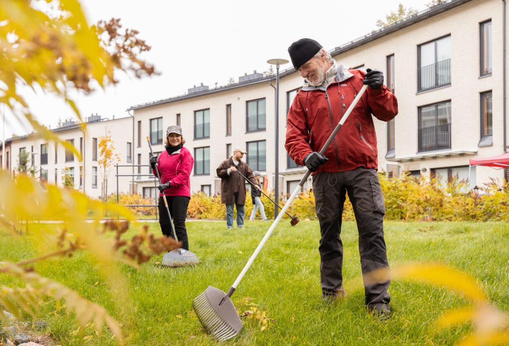 Ihmisiä haravoimassa syksyisellä pihalla. Etualalla punatakkinen mies.