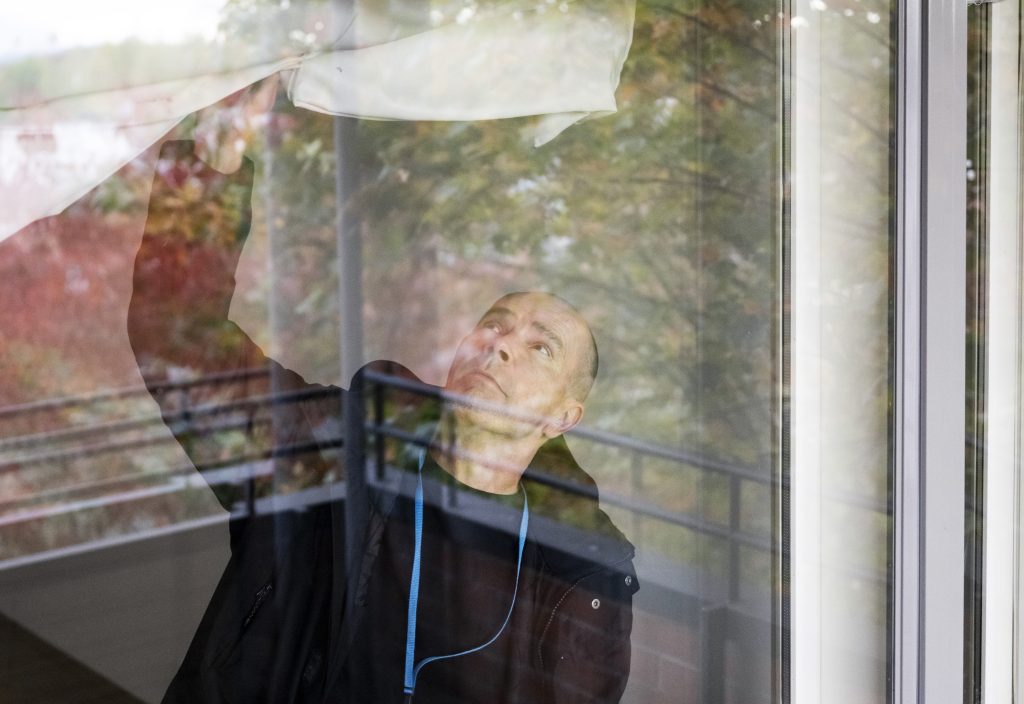 Asunnontarkastaja Markku Pitkänen kuvattuna ikkunan läpi. Hän pitelee valkoista verhoa.
