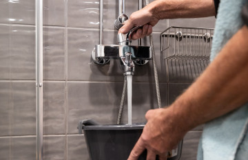 Seinässä olevasta hanasta valutetaan vettä sankoon.