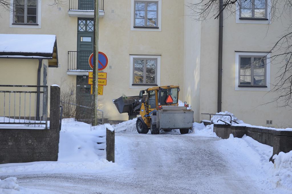 Lumityökone kulkee kerrostalon pihalla.