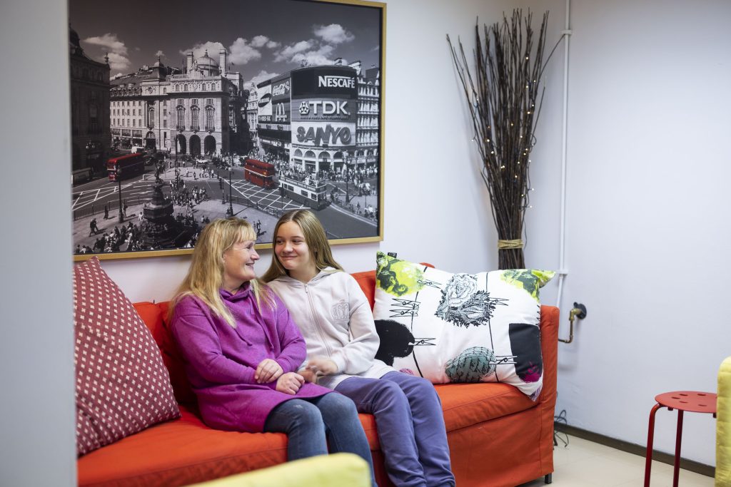 A woman and a girl are sitting on a sofa and looking at each other smiling.