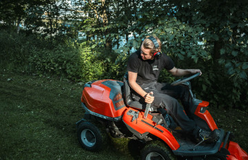 Atte Railo istuu oranssissa päältä ajettavassa ruohonleikkurissa vihreässä maisemassa.