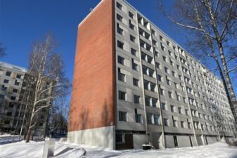 Korkea kerrostalo lumisella pihalla.