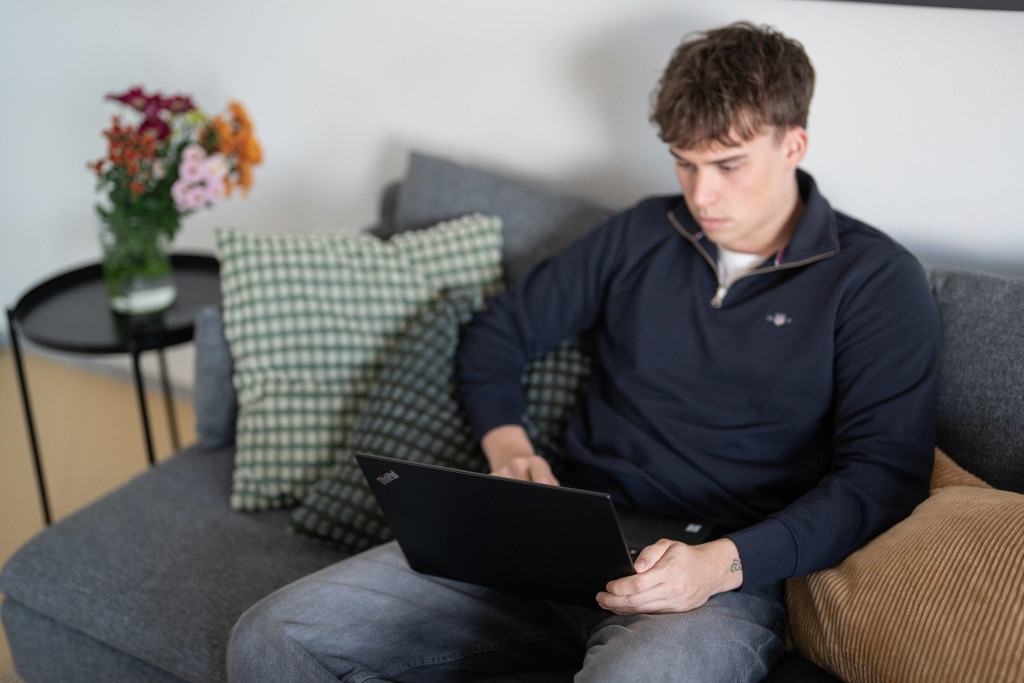 Mies käyttää kannettavaa tietokonetta sohvalla.