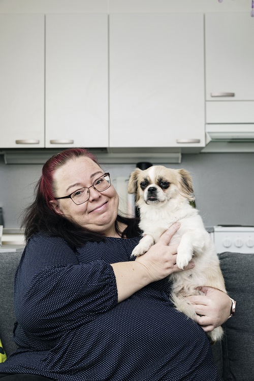 Sari Lindfors sits on the couch with Maisa, the Tibetan Spaniel, in her lap.