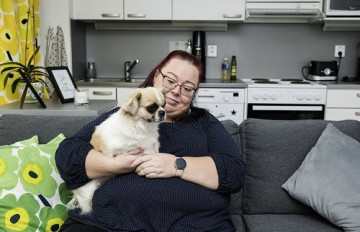 Sari Lindfors sits on the couch with Maisa, the dog, in her lap.