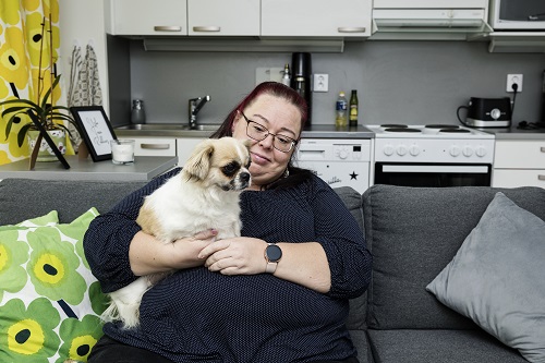 Sari Lindfors sits on the couch with Maisa, the dog, in her lap.