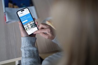 En person håller i en smarttelefon där Hekas webbplats visas på skärmen.