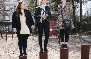 Kolme naista ulkona katsoo toisiaan ja hymyilee.