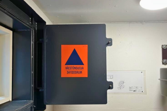 Ikkunaluukku, jossa on väestönsuojan oranssi-sininen merkki.