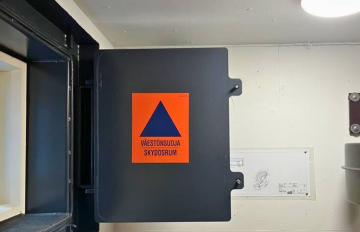 Ikkunaluukku, jossa on väestönsuojan oranssi-sininen merkki.