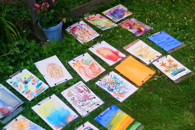 Värikkäitä paperille maalattuja teoksia nurmikolla.