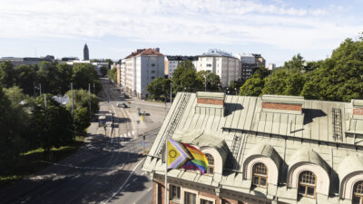 Pride-lippu liehuu Hekan toimiston pihalla. Taustalla näkyy Alppilaa.