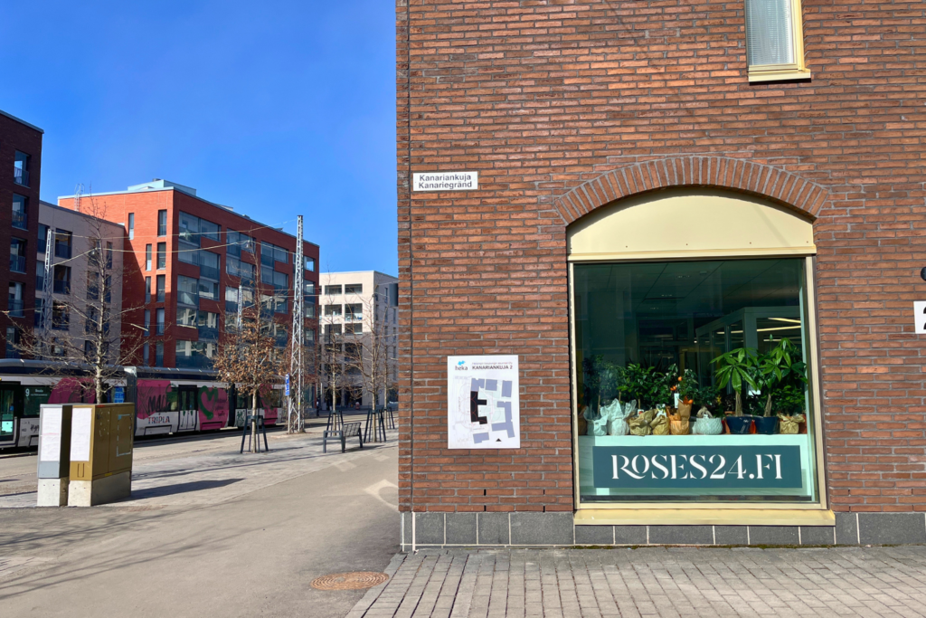 Roses24.fi-kukkakaupan Kanariankujan puoleinen ikkuna. Taustalla näkyy katunäkymä ja ohi kulkeva ratikka.