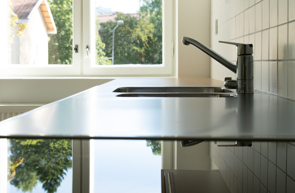 Induktiolieden pinta ja tiskipöytä, joilta heijastuu ulkona näkyvät vihreät puut.