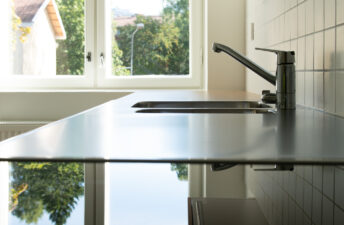 Induktiolieden pinta ja tiskipöytä, joilta heijastuu ulkona näkyvät vihreät puut.