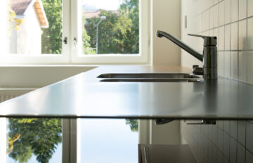 Induktiolieden pinta ja tiskipöytä, joilta heijastuu ulkona näkyvät vihreät puut.