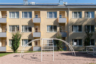 Keltainen kolmikerroksinen kerrostalo, jonka edessä leikkipaikka.