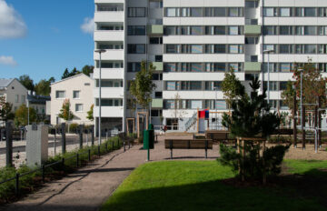 Kerrostalon piha-alue, jossa on istutuksia, penkkejä ja leikkipaikka.