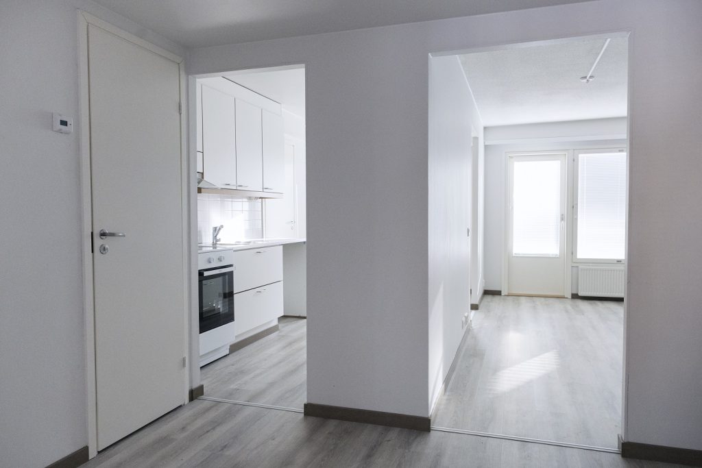 The picture shows a kitchen on the left and another room next to it. There are no doors between the rooms. The door to the bathroom is on the wall next to the kitchen doorway.