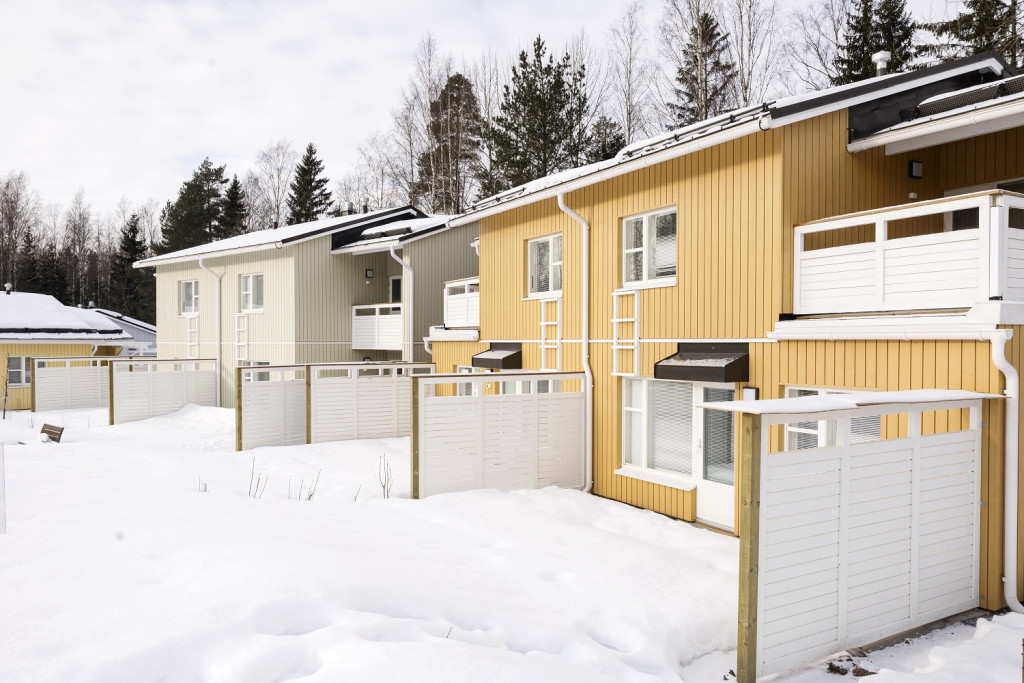 På bilden finns ett gult och ett ljusgrått hus fotograferade från innergården på Husfolksvägen 10. På gården finns snö. 