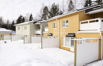 På bilden finns ett gult och ett ljusgrått hus fotograferade från innergården på Husfolksvägen 10. På gården finns snö. 