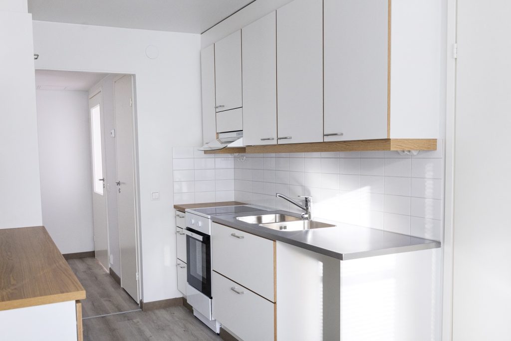 Kuva asunnon remontoidusta keittiöstä, jossa tiskipöytä, valkoiset kaapistot, uuni ja astianpesukone. 