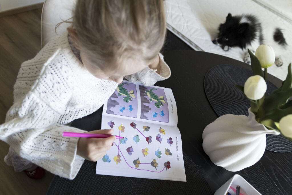 En flicka sitter vid köksbordet och ritar i en pysselbok.