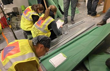 Huomioliiveihin pukeutuneet osallistujat rakentavat kerrossänkyjä väestönsuojassa.