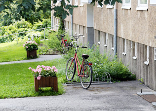 Kesäinen kerrostalon piha, jossa polkupyörä ja kukkaistutuksia.