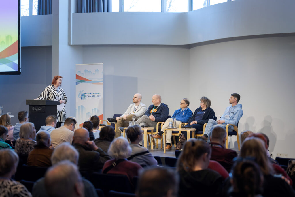 Paneelikeskustelu lavalla, keskustelijat istuvat tuoleilla yleisön edessä.